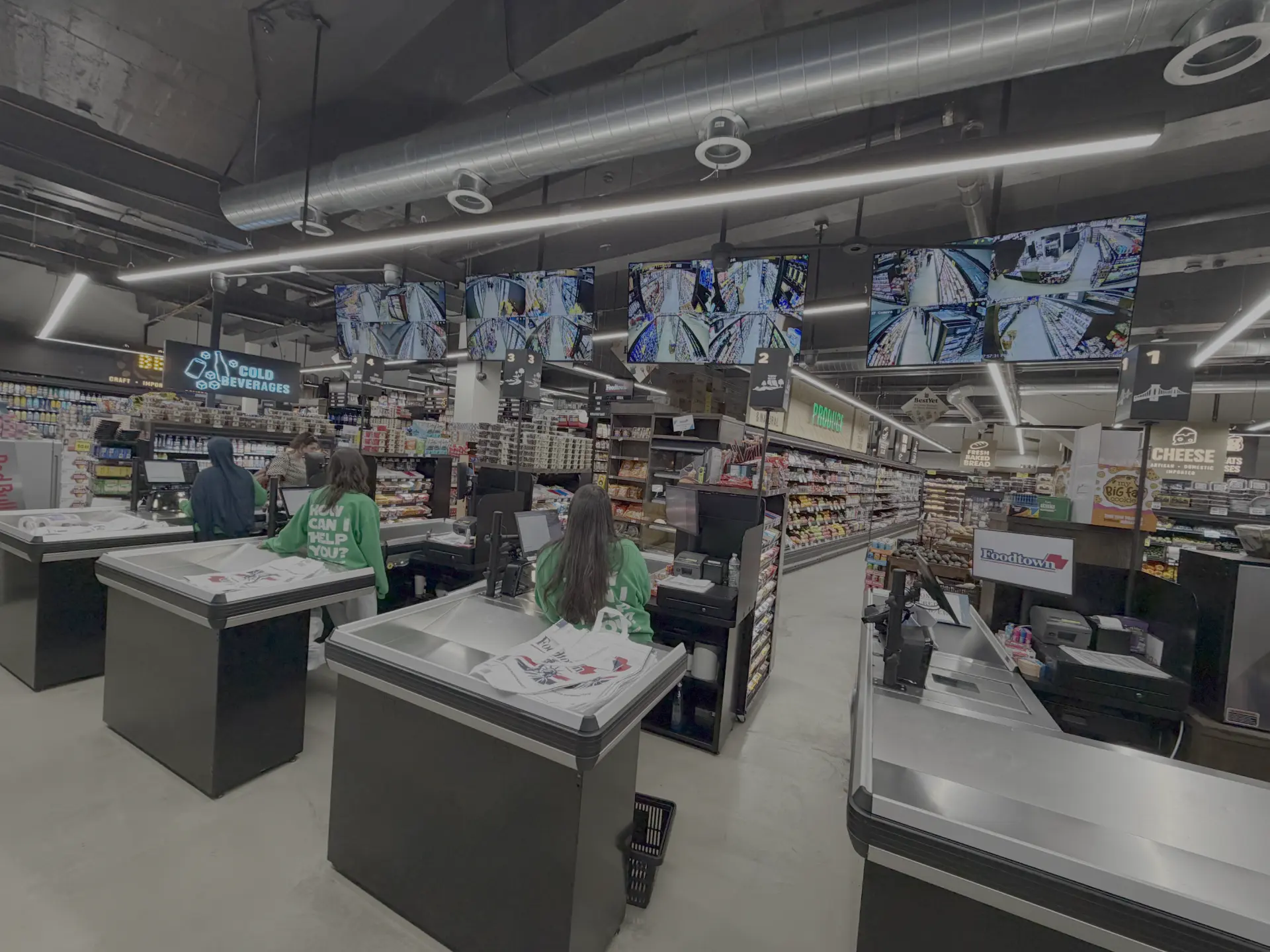 Supermarket checkout counter with registers, monitors, and staff assisting customers